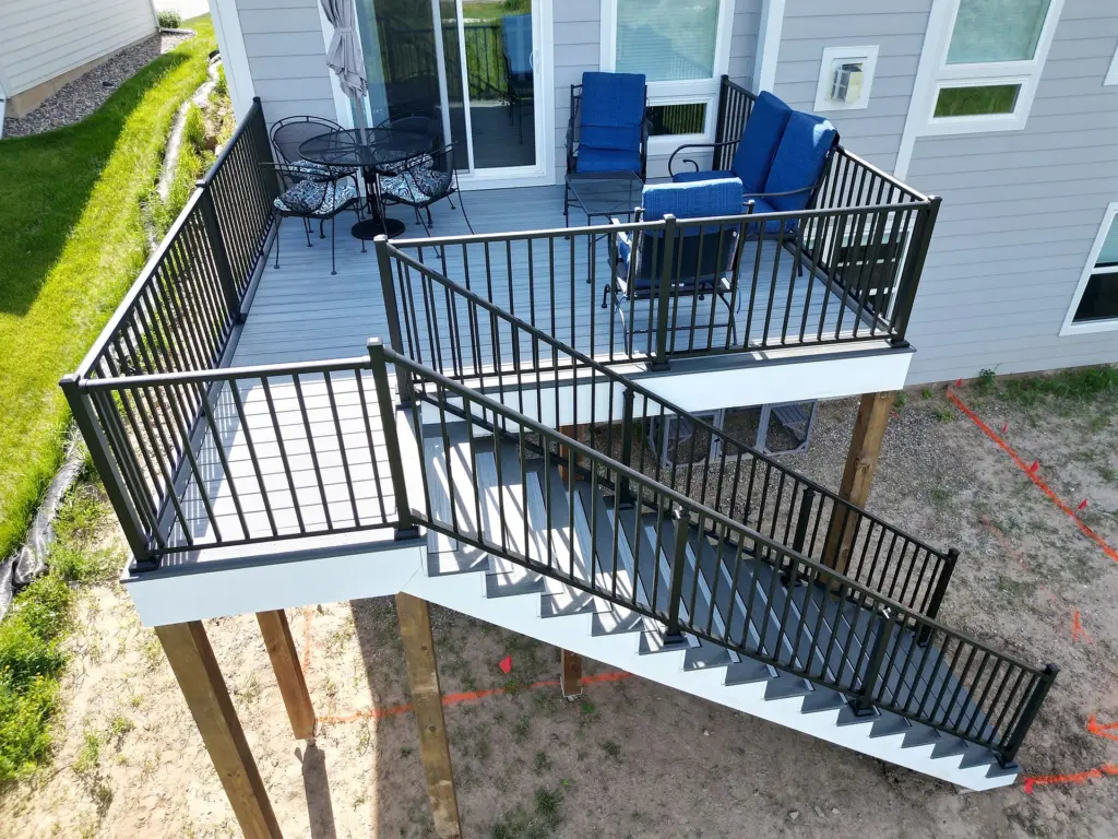 elevated-gray-composite-deck-with-black-metal-railings-with-outdoor-living-blue-chairs-and-glass-table-with-sliding-glass-doors-in-gray-big-house-in-twin-cities-mn